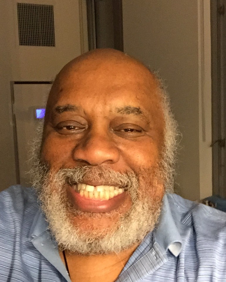 A senior Black man with a white and gray beard smiles at the camera.