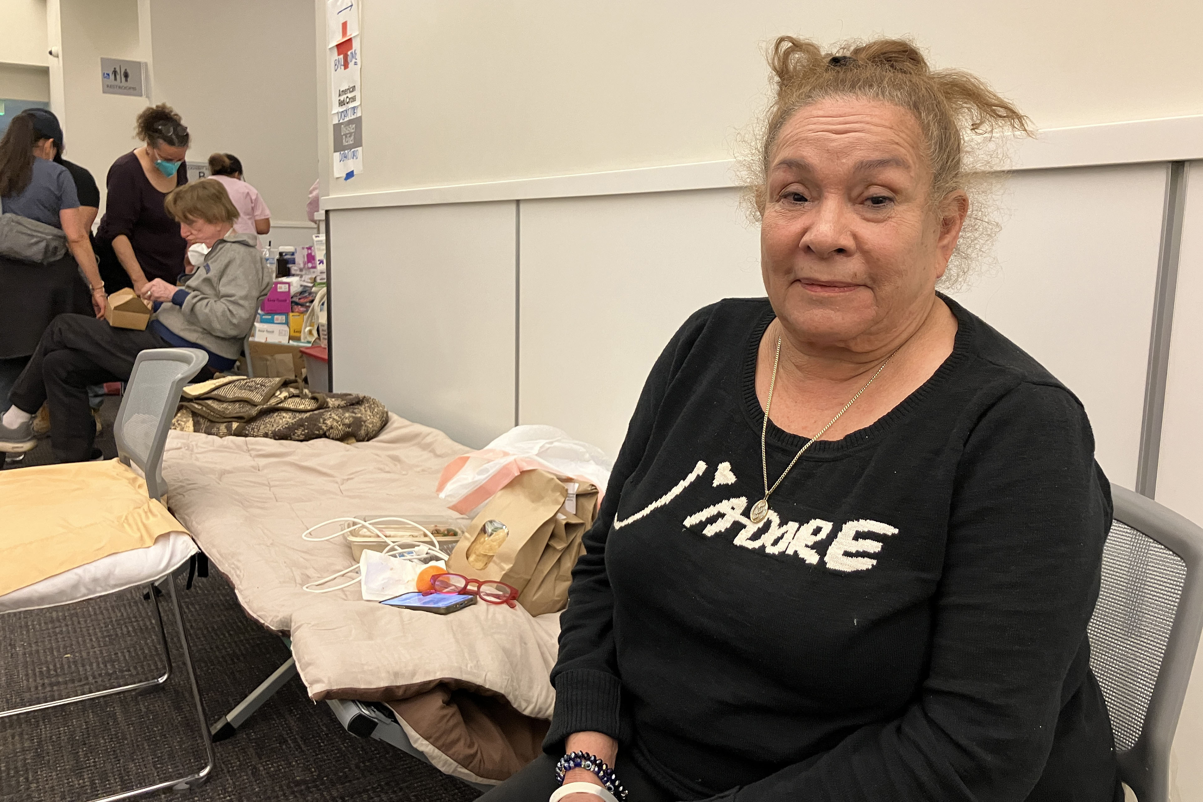 A woman in a black shirt poses for a photo in a chair next to a cot