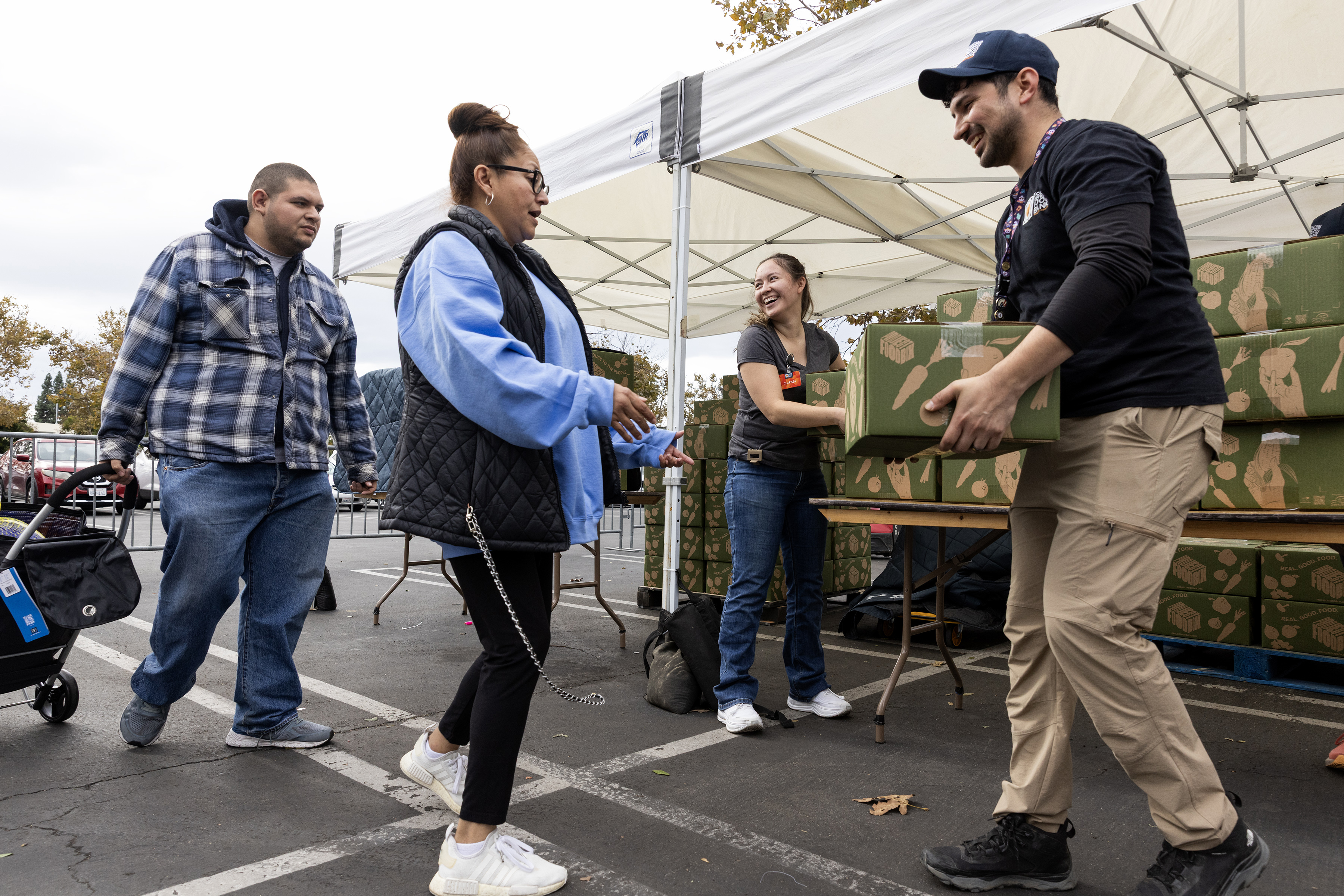A photo of two people on the left of the frame receiving boxes of food from two food bank workers on the right.